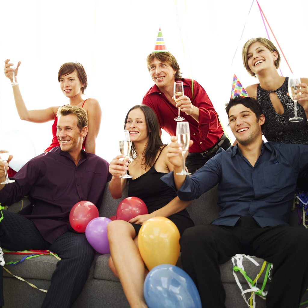 Group of six people, wearing party hats, raising their glasses.
